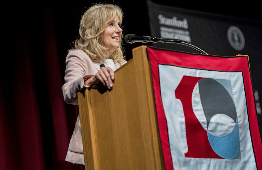 Jill Biden speaking on a podium with Stanford GSE 100 logo