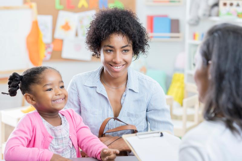A mom and daughter speaking with a female teacher in a classroom