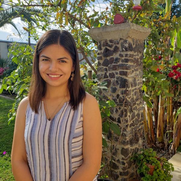 Belen Gutierrez, outside in front of flowering plants, smiling